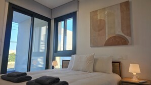 Une chambre d’hôtel avec un grand lit, deux lampes de chevet, un tableau au mur et une vue par la fenêtre.