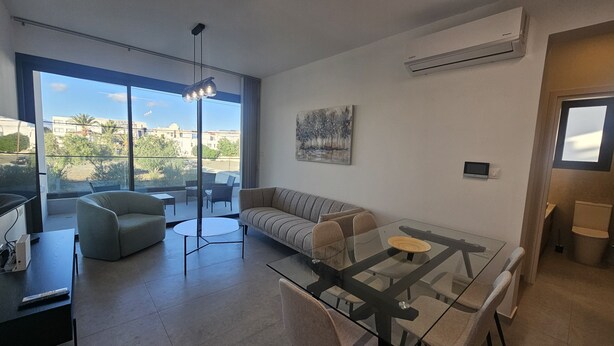 Un salon moderne avec une table à manger en verre, un canapé et une grande fenêtre donnant sur la ville.