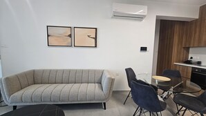Ett modernt vardagsrum med en soffa, två fåtöljer, ett litet bord och en köksdel med en spis och en mikrovågsugn.