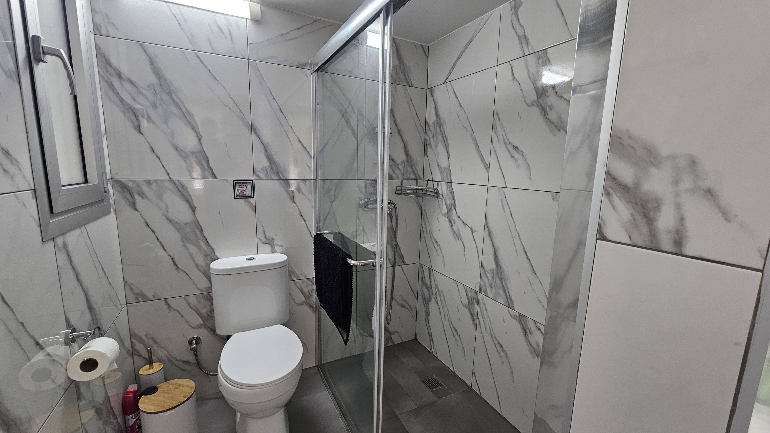 A modern bathroom with a toilet, bidet, and shower stall, all with marble tile walls.