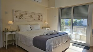 Une chambre à coucher comprenant un lit, deux tables de chevet, une commode, une grande fenêtre avec stores et une vue sur l’extérieur.
