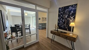 Un salon moderne avec une porte vitrée donnant sur un espace repas. On y trouve une console sur laquelle sont posés une lampe et des objets décoratifs.