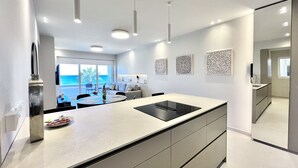 A modern kitchen with a central island, pendant lighting, and a view of the ocean. - 14 LCA - Stay Atalanta Apartment (Larnaca)