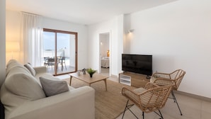 A modern living room with a sofa, coffee table, wicker chairs, a flat-screen TV, and a sliding glass door leading to a balcony. - Villa Los Altos Alene 10B by Escape Home (Playa Blanca)