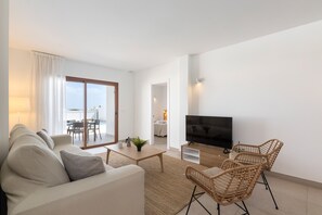 Un salon moderne comprenant un canapé, une table basse, des fauteuils en osier, un téléviseur à écran plat et une porte-fenêtre coulissante donnant sur un balcon.