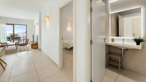 Een moderne hotelkamer met een zithoek, een badkamer met een grote spiegel en wastafel, en uitzicht op de stad.