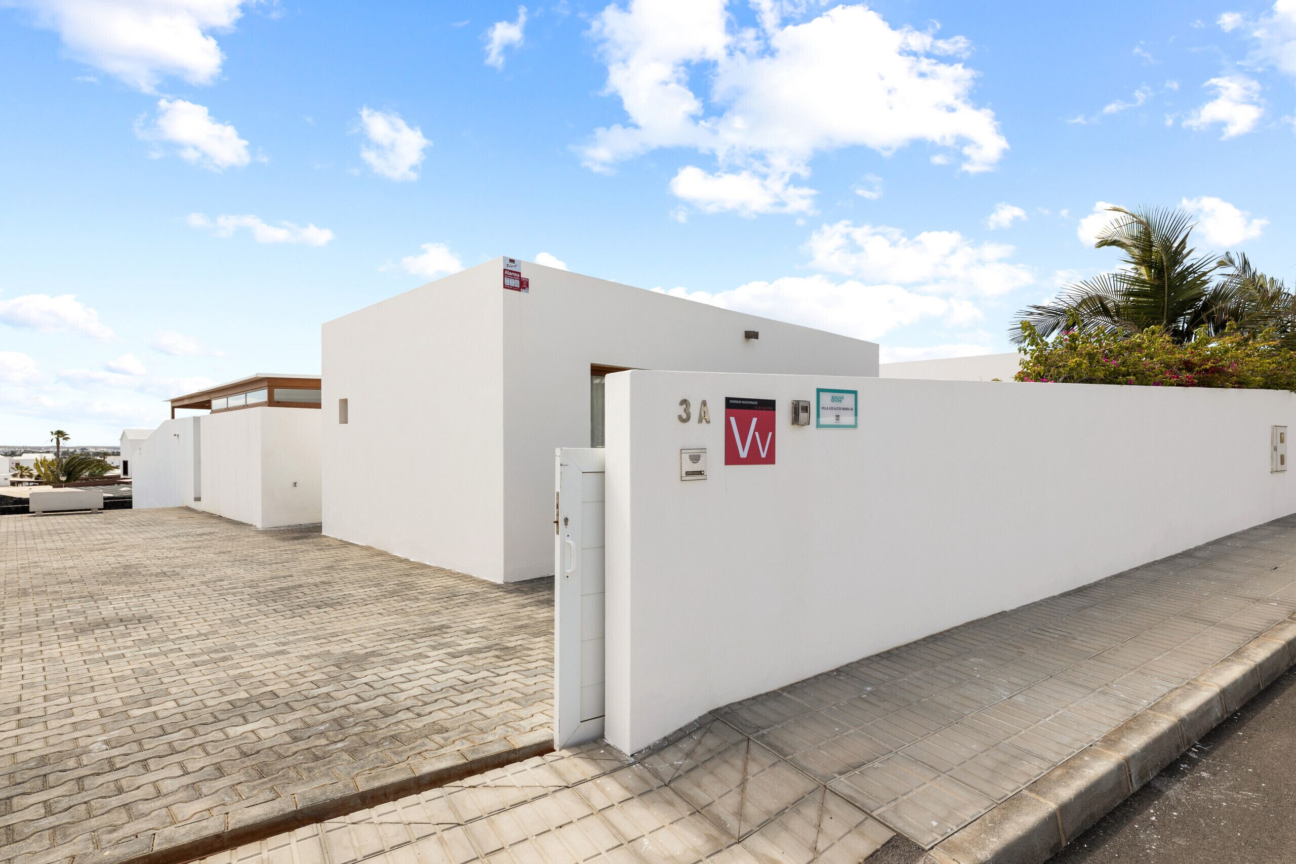 Een modern gebouw met een witte gevel, een verhard entreegebied en een kleine deur met een rood ‘W’-bord.
