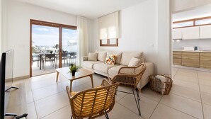 Un salon moderne avec un canapé, deux fauteuils en osier, une table basse et un téléviseur.