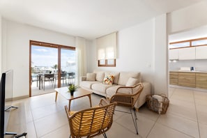 Una sala moderna con un sofá, dos sillones de mimbre, una mesa de centro y un televisor.
