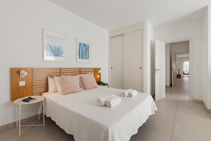 Un dormitorio con cabecera de madera, una mesita de noche con lámpara, y una cama con sábanas blancas y toallas enrolladas.