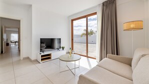 Un salon moderne doté d’un téléviseur à écran plat, d’un canapé, d’une petite table et d’une grande fenêtre donnant sur la plage.