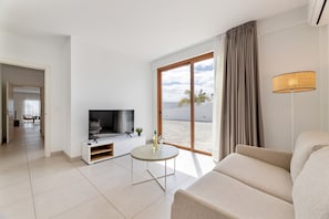 Una sala de estar moderna con un televisor de pantalla plana, un sofá, una mesita y un ventanal con vistas a la playa.