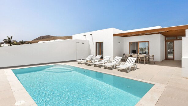 A swimming pool with lounge chairs, a patio area with a table and chairs, and a mountain in the background. - Villa Los Altos Yaiza 9A by Escape Home (Playa Blanca)