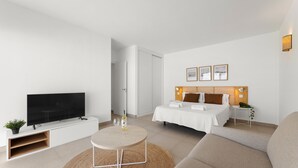 A modern hotel room with a flat-screen TV, a round dining table, a sofa, a bed with a wooden headboard, and a small side table. - Villa Los Altos Yaiza 9A by Escape Home (Playa Blanca)