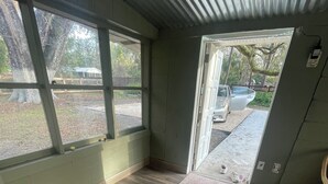 A room with large windows, a wooden floor, and a door leading outside.