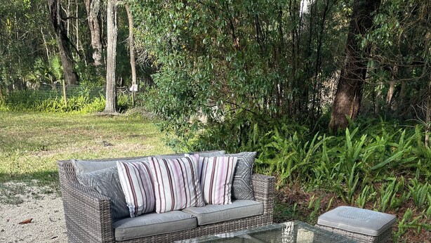 A wicker outdoor sofa set with cushions and a glass-top coffee table, placed on gravel.