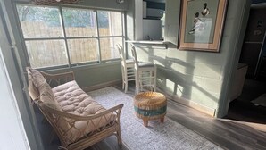A room with a large window, a wicker chair, a small table, and a patterned rug.