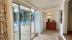 Un couloir avec une porte vitrée donnant sur un espace extérieur aménagé avec des chaises et une piscine.