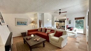 Un salon avec un canapé rouge, un canapé blanc, une table basse en bois et un ventilateur de plafond.
