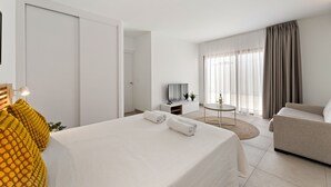 Ein Hotelzimmer mit Bett, Sofa, Fernseher, kleinem Tisch und einem Fenster mit Vorhängen.