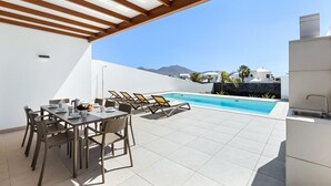 Eine Außenpatio mit Pool, Esstisch, Stühlen und Liegestühlen.