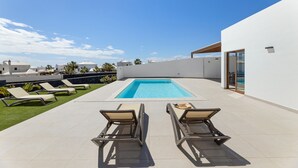 A rooftop pool with lounge chairs, a clear sky, and a modern building with a glass door.