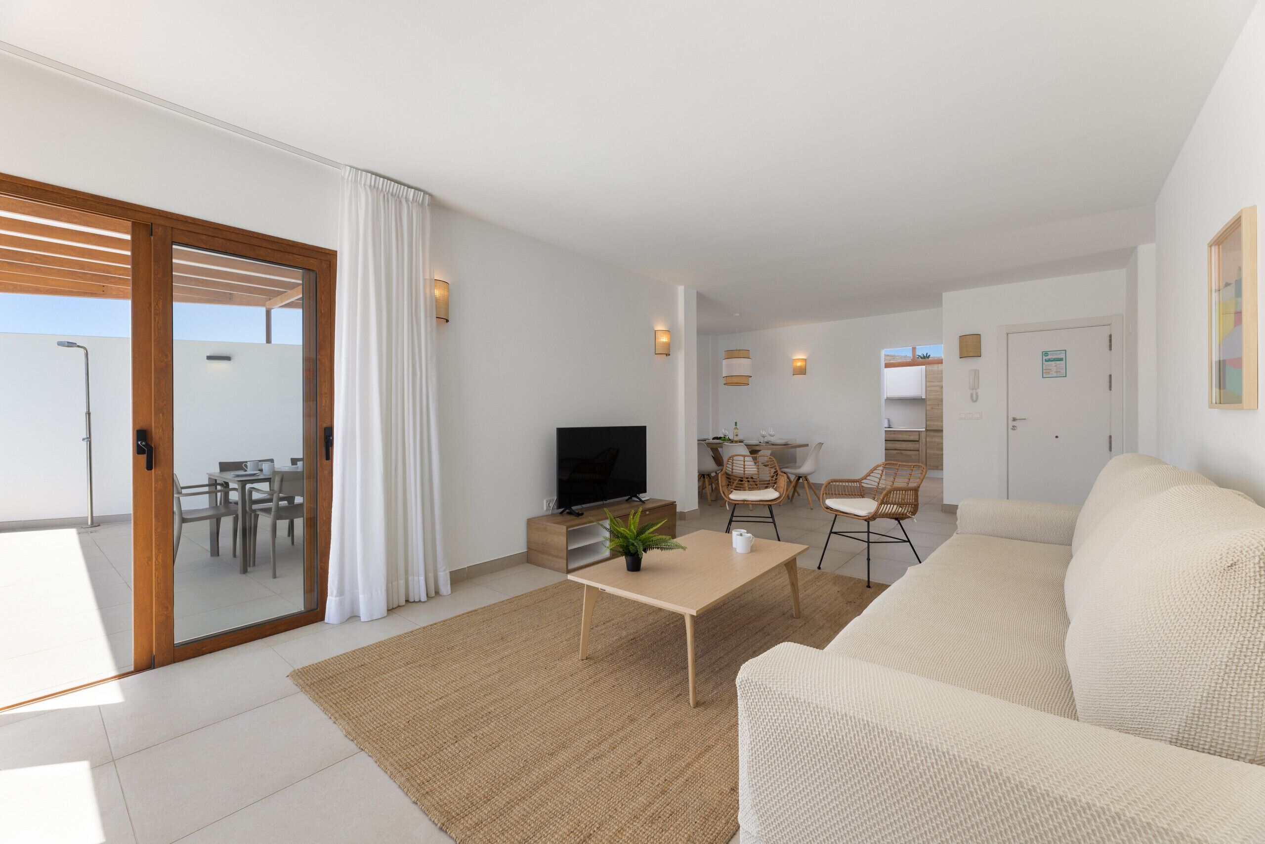 Una sala de estar moderna con un sofá, una mesa de centro y un televisor. Hay un comedor con sillas y una mesa, y una cocina con armarios y una encimera.