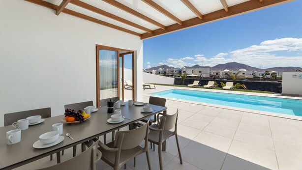 A dining area with a table set for four, overlooking a swimming pool and mountains.