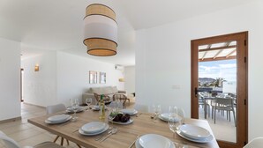 A dining area with a wooden table set for six, white plates, and a bottle of wine.
