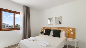 A hotel room with a bed, a small table, a window with curtains, and two framed pictures on the wall.