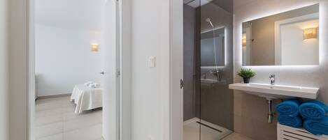 A modern bathroom with a glass shower enclosure, a white sink with a mirror, and a towel rack with towels.