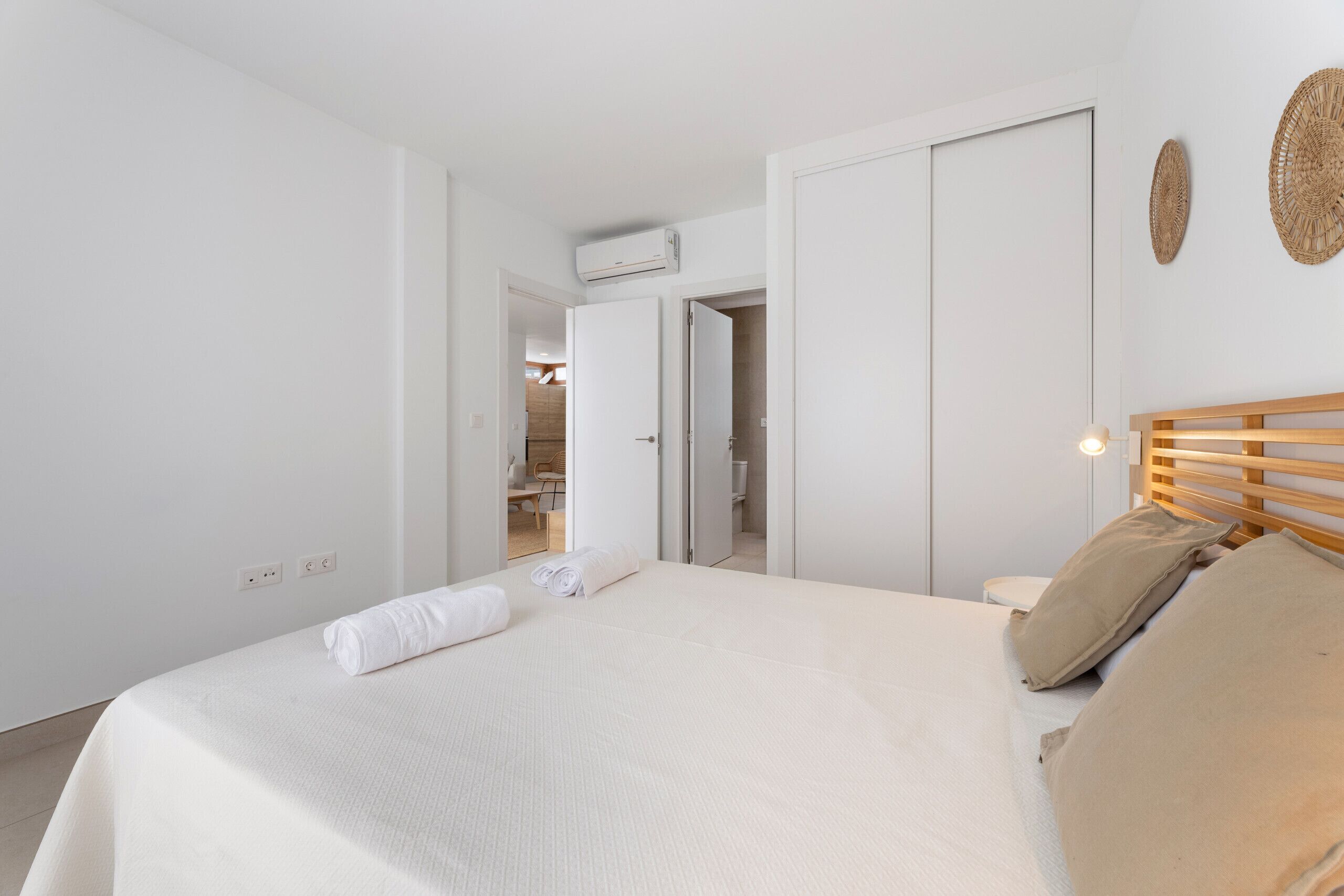 Een slaapkamer met een bed, een houten hoofdbord, een wandairconditioner en een deur naar een andere kamer.