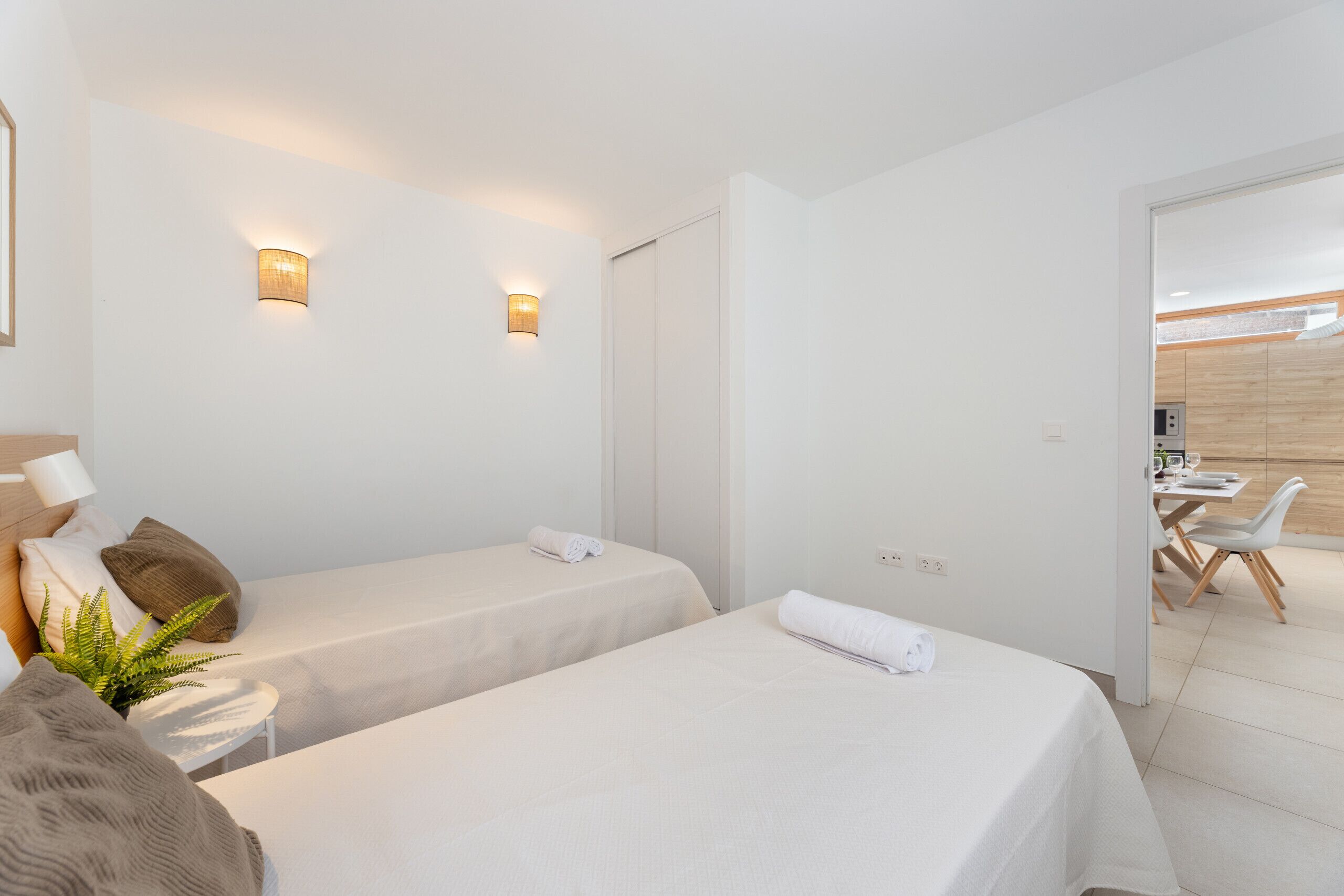 Een hotelkamer met twee bedden, een kleine tafel met een plant, en een eetgedeelte zichtbaar door een open deur.