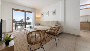 En moderne stue med sofa, to fletstole, et spisebord og udsigt til det fri.