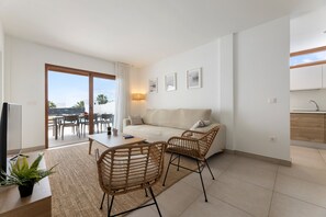 Una sala moderna con sofá, dos sillones de mimbre, una mesa de comedor y vistas al exterior.