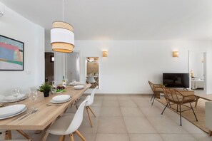 Un comedor moderno con una mesa de madera, sillas blancas y un televisor al fondo.
