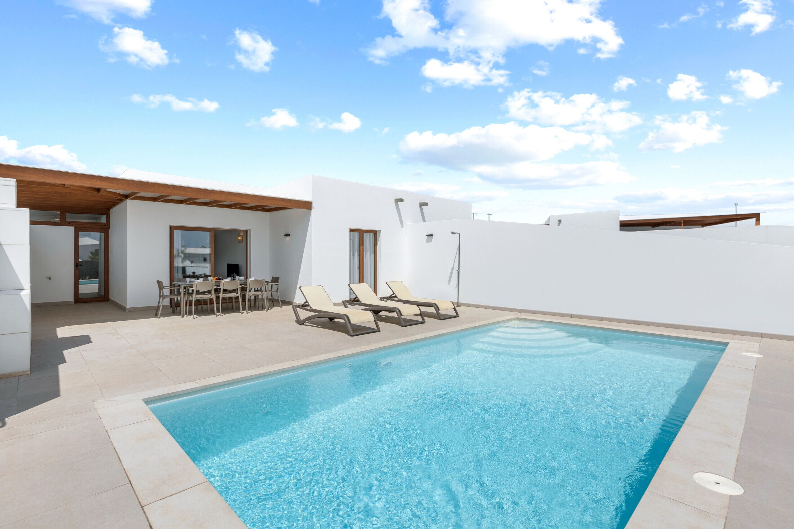 A swimming pool with lounge chairs, a table with chairs, and a covered outdoor area.