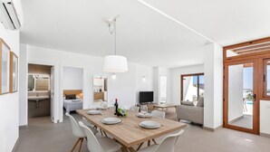 A modern dining area with a wooden table and white chairs, a television, and a view of the outdoors. - Villa Los Altos Deva 12A by Escape Home (Playa Blanca)