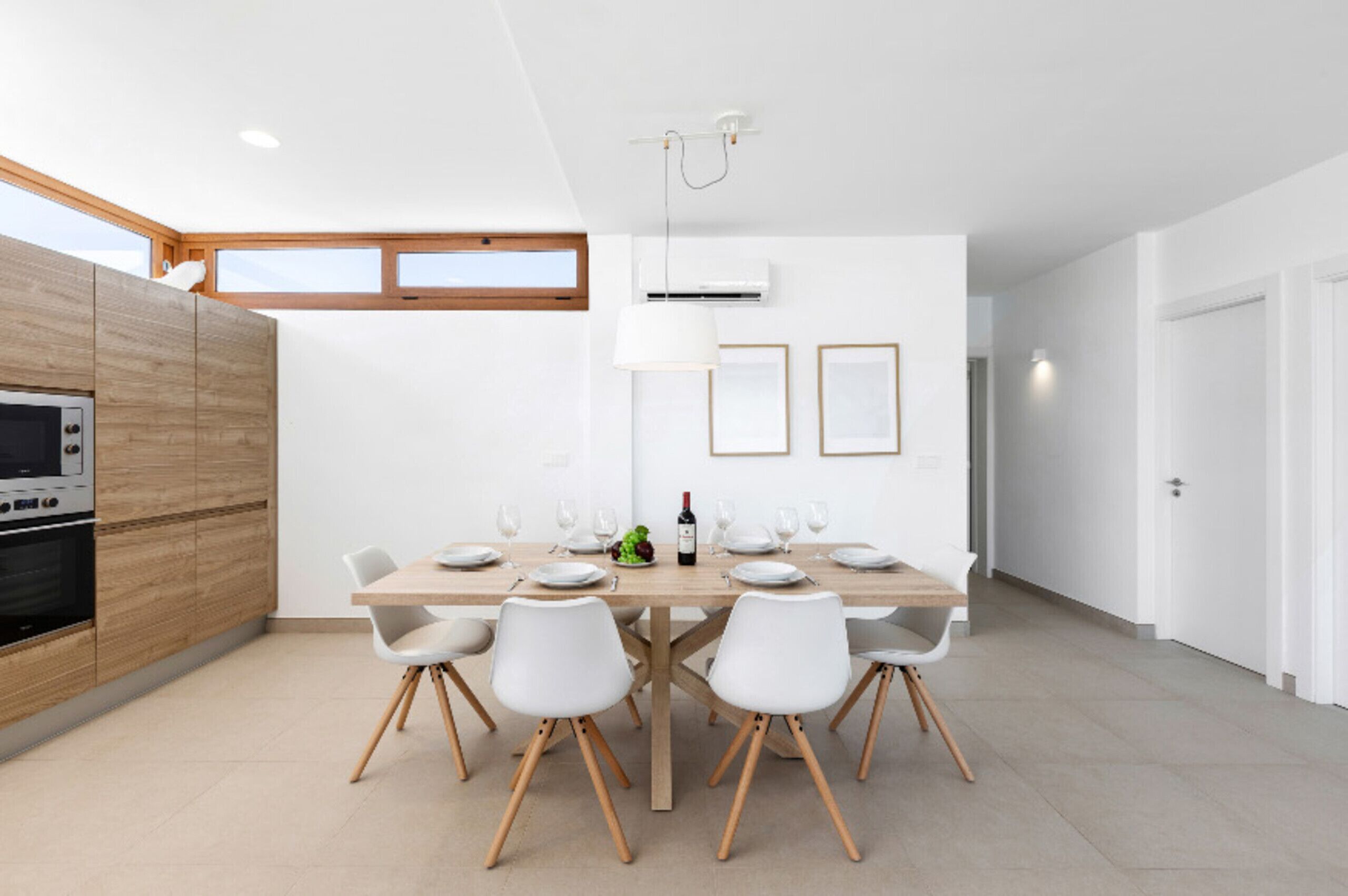 Eine moderne Küche mit Holzschränken, einem eingebauten Backofen und einem Essbereich mit Holztisch und weißen Stühlen.