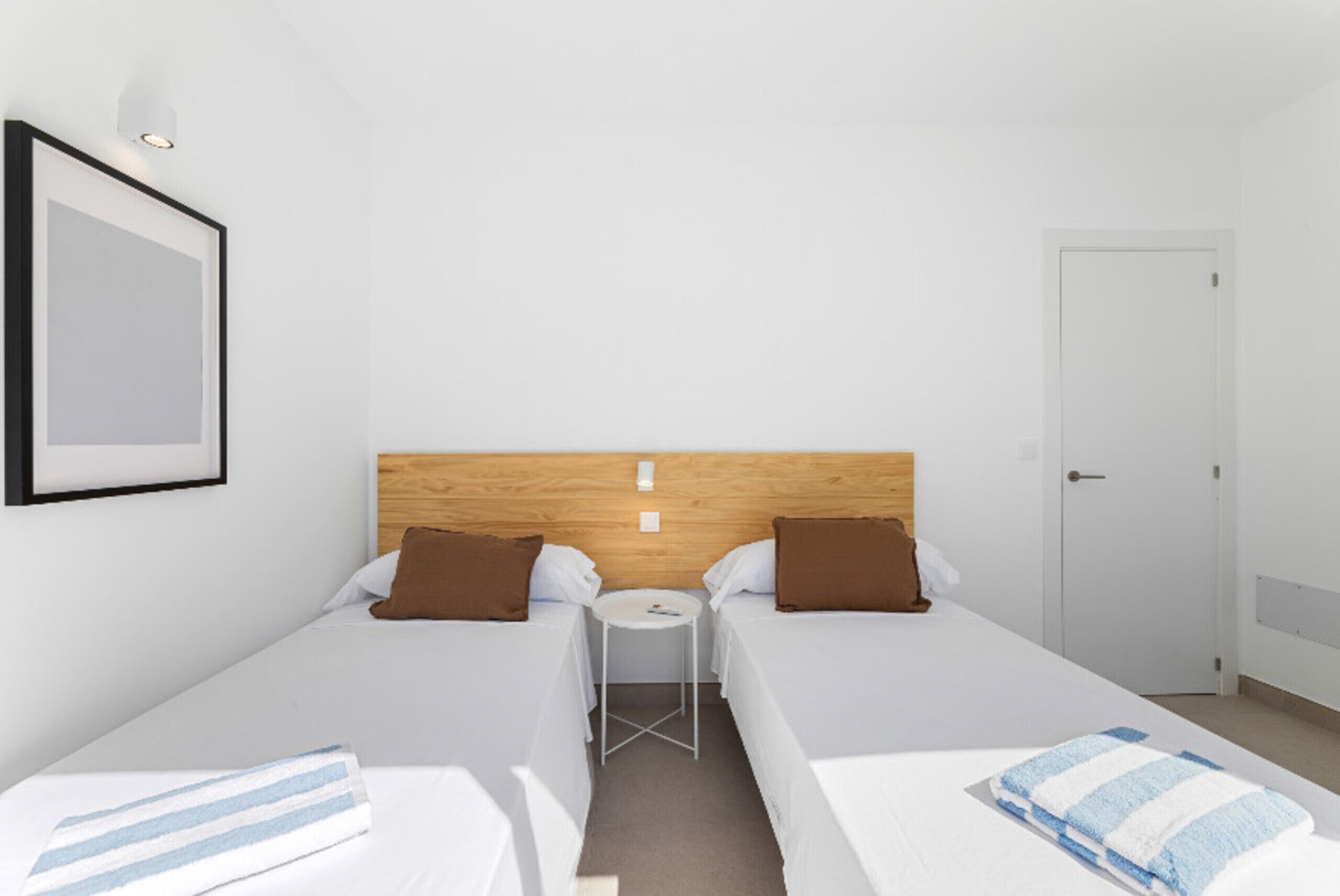 Ein Hotelzimmer mit zwei Einzelbetten, einem kleinen Tisch, einem gerahmten Bild an der Wand und einer Tür.