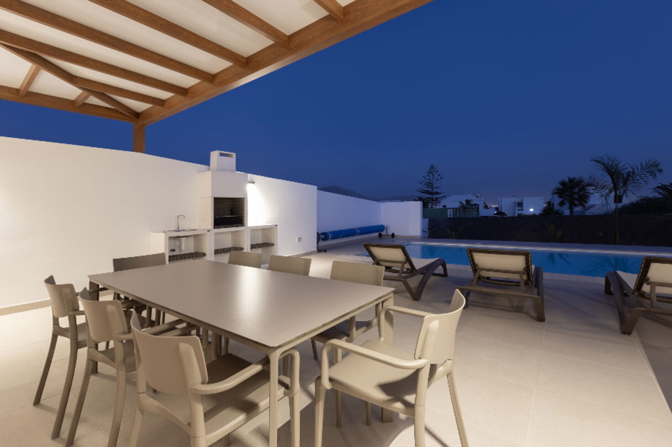An outdoor dining area with a pool, a covered patio, and a kitchen area.