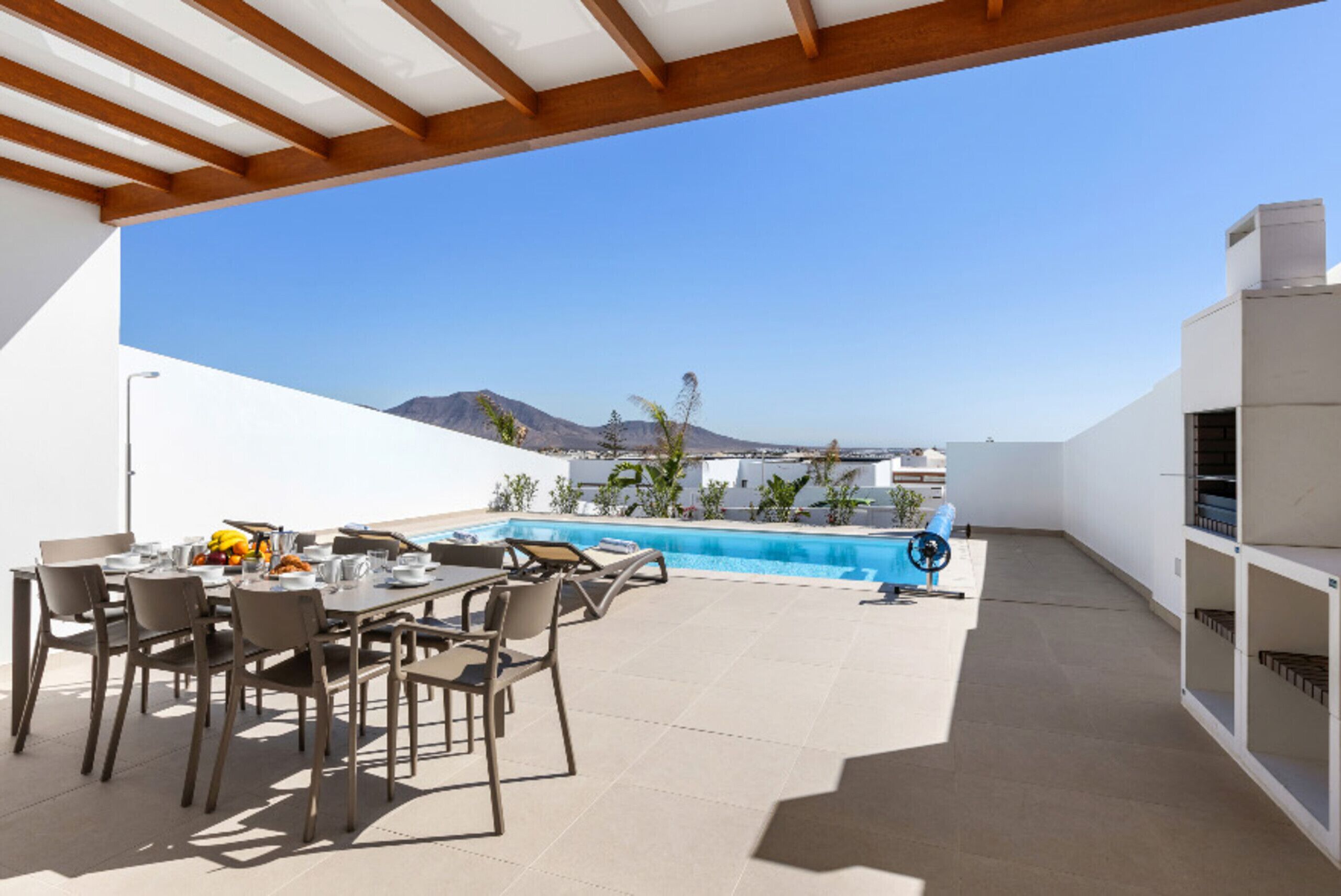 An outdoor dining area with a pool, chairs, and a table set for a meal.