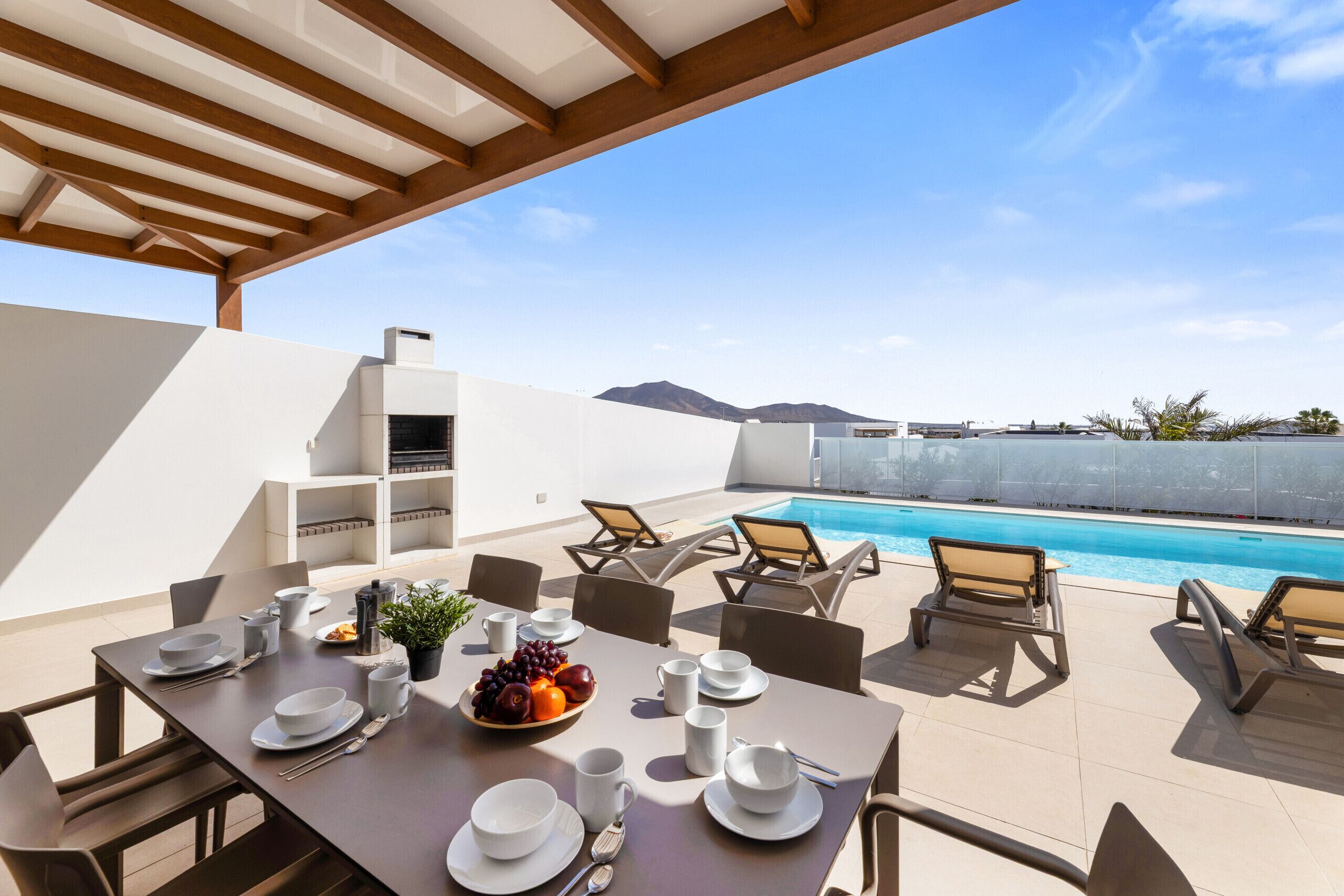 Comedor con mesa dispuesta para cuatro, piscina y sillas de descanso.