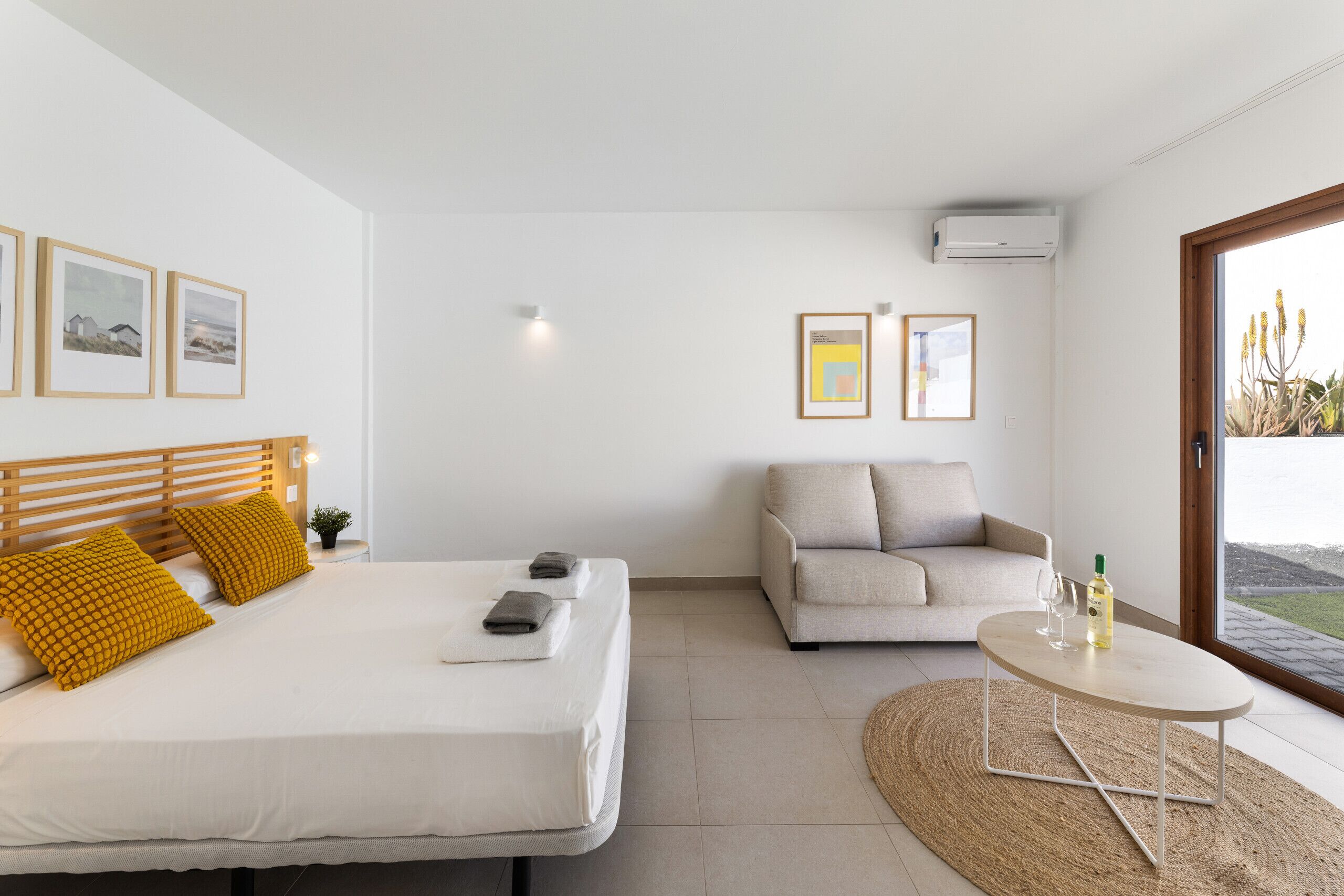 Ein modernes Schlafzimmer mit Bett, Sofa, einem kleinen Tisch und Blick ins Freie.