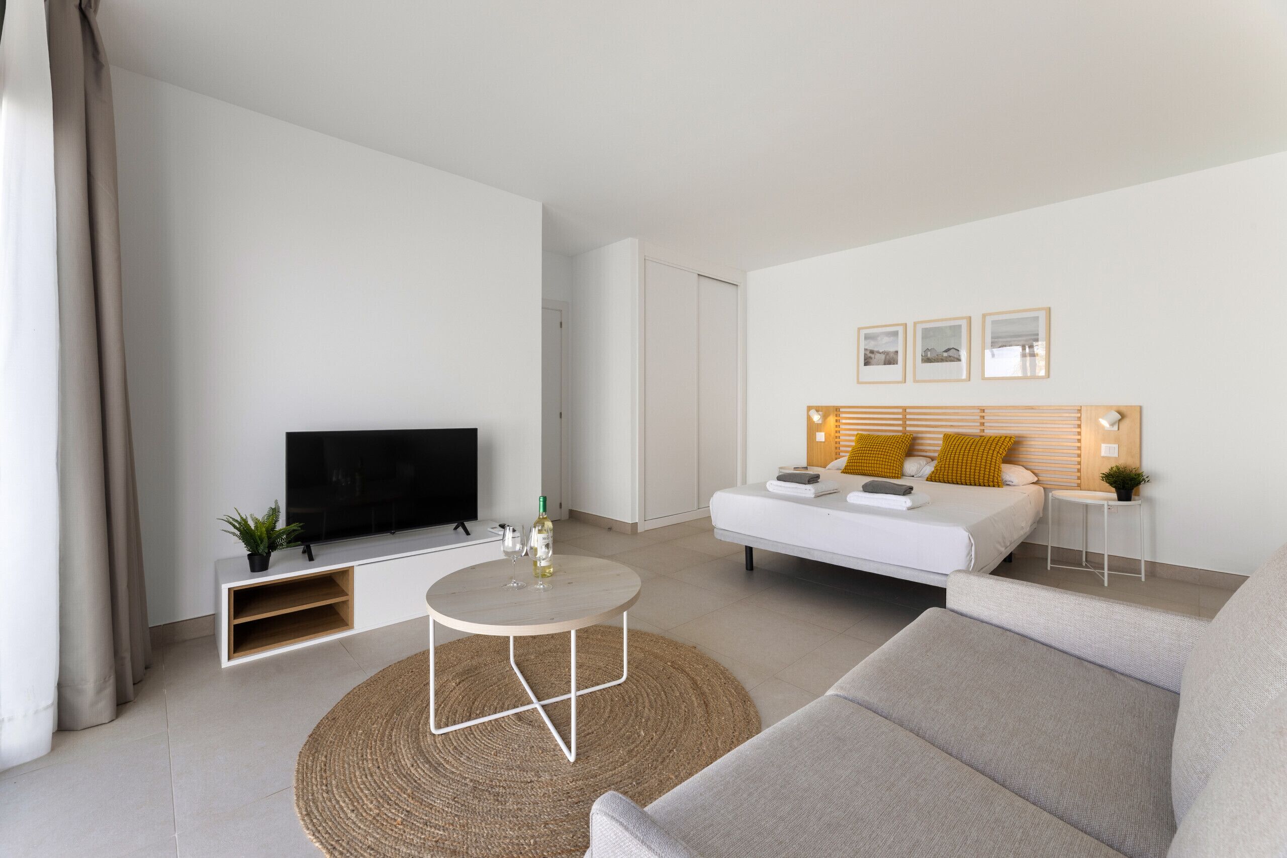 A modern living room with a flat-screen TV, a white sofa, a round coffee table, and a small side table with a lamp.
