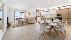A modern kitchen with white cabinets, a dining table set for four, and a large window. - Villa Los Altos Blanca 8A by Escape Home (Playa Blanca)