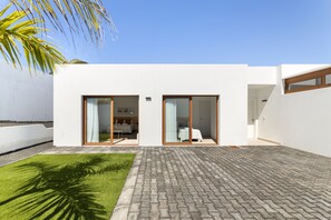 Une maison moderne dotée d’un patio dallé, d’une pelouse et d’une grande fenêtre.
