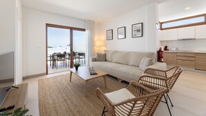 A modern living room with a sofa, coffee table, and wicker chairs, a dining area with a table and chairs, a kitchen with wooden cabinets, and a balcony with a view. - Villa Los Altos Blanca 8A by Escape Home (Playa Blanca)