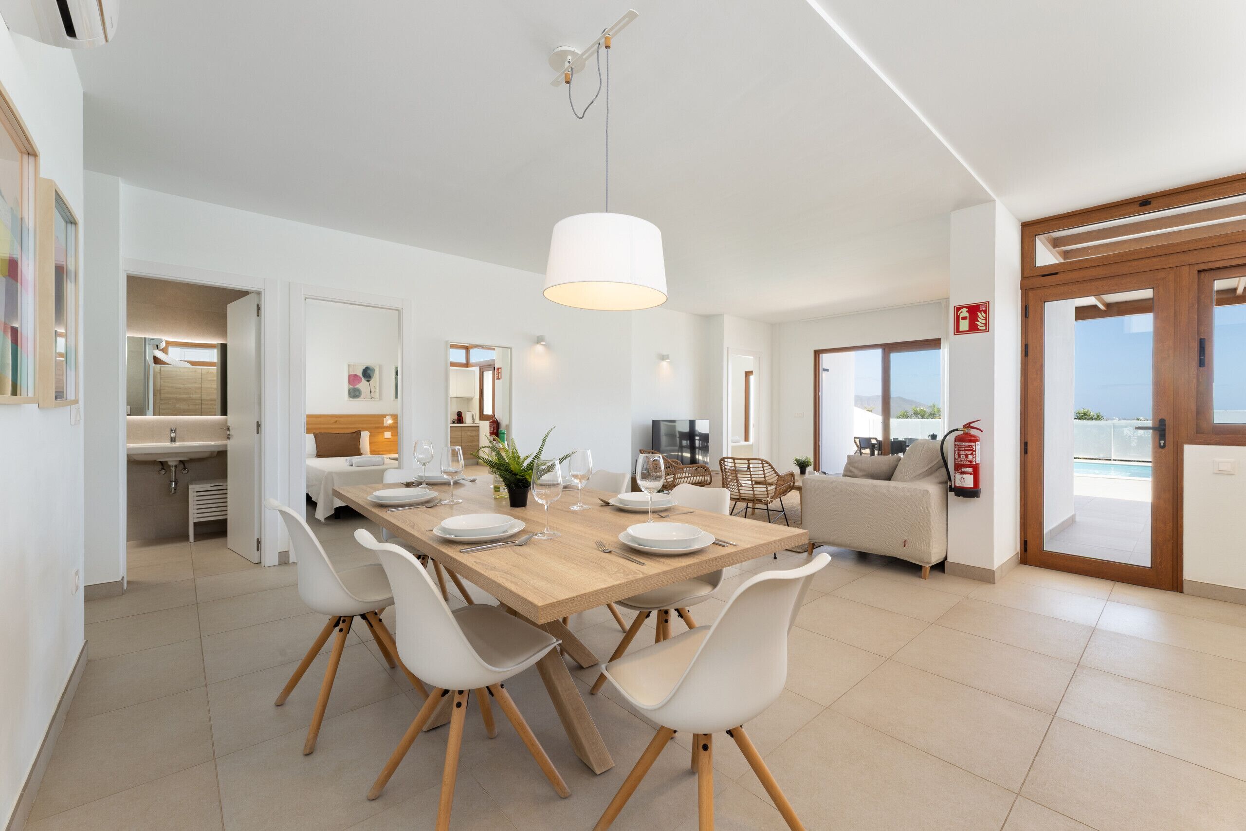 Un espace repas moderne avec une table en bois, des chaises blanches et un luminaire suspendu.