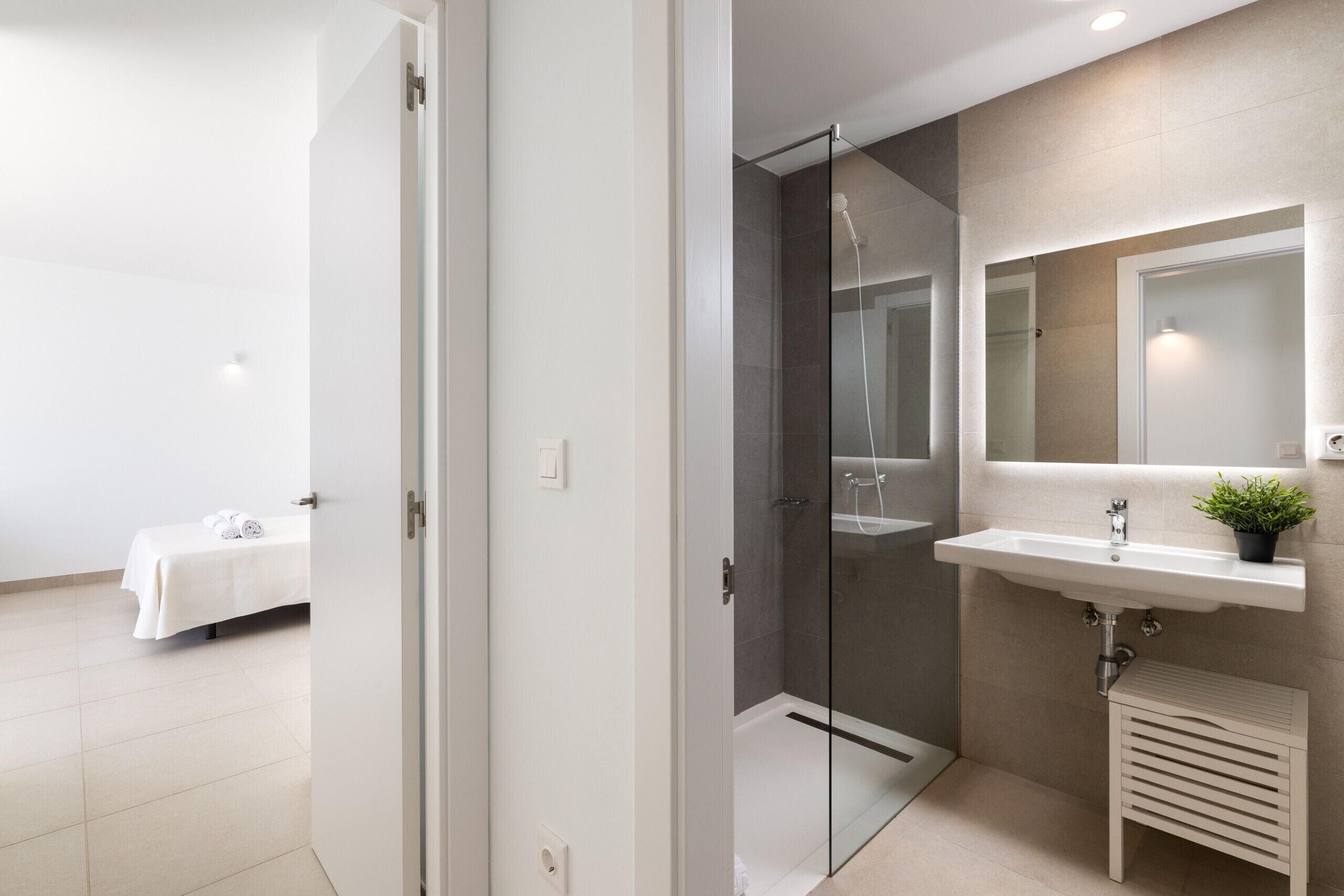 Un baño moderno con cabina de ducha de vidrio, un lavamanos con espejo y un taburete pequeño.